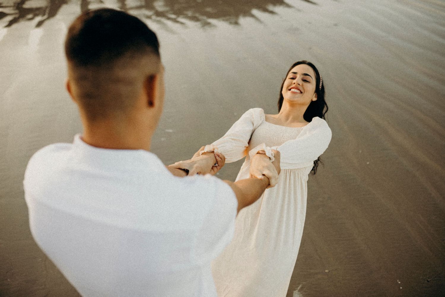 A playful couple spins and dances together on a sandy beach.