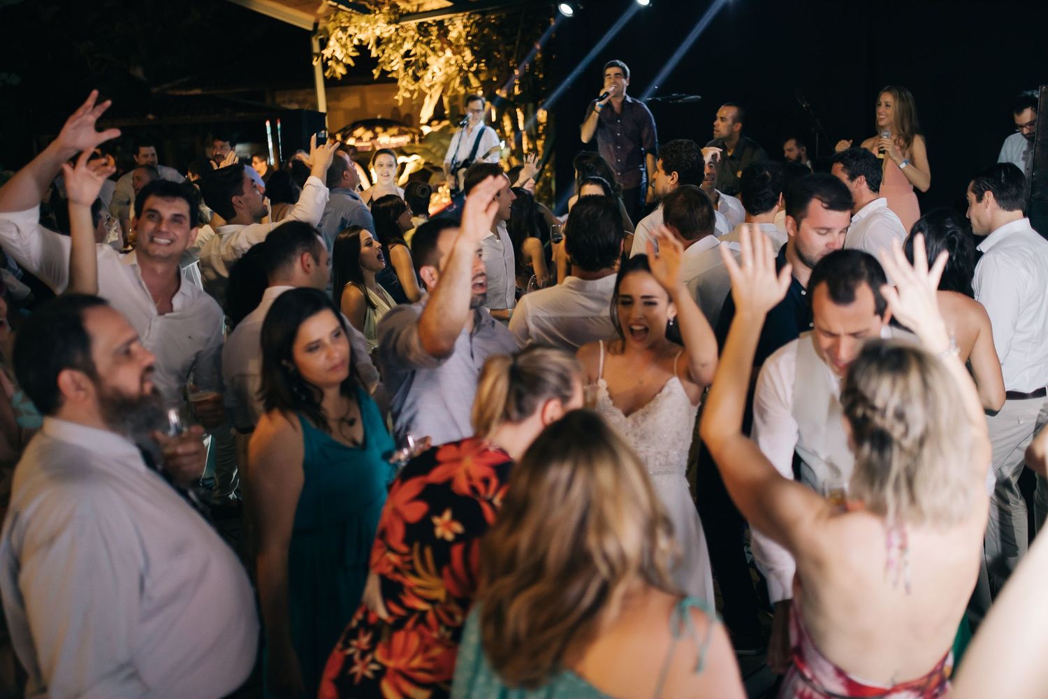 Energetic wedding guests dancing and celebrating on a crowded dance floor with party lighting.