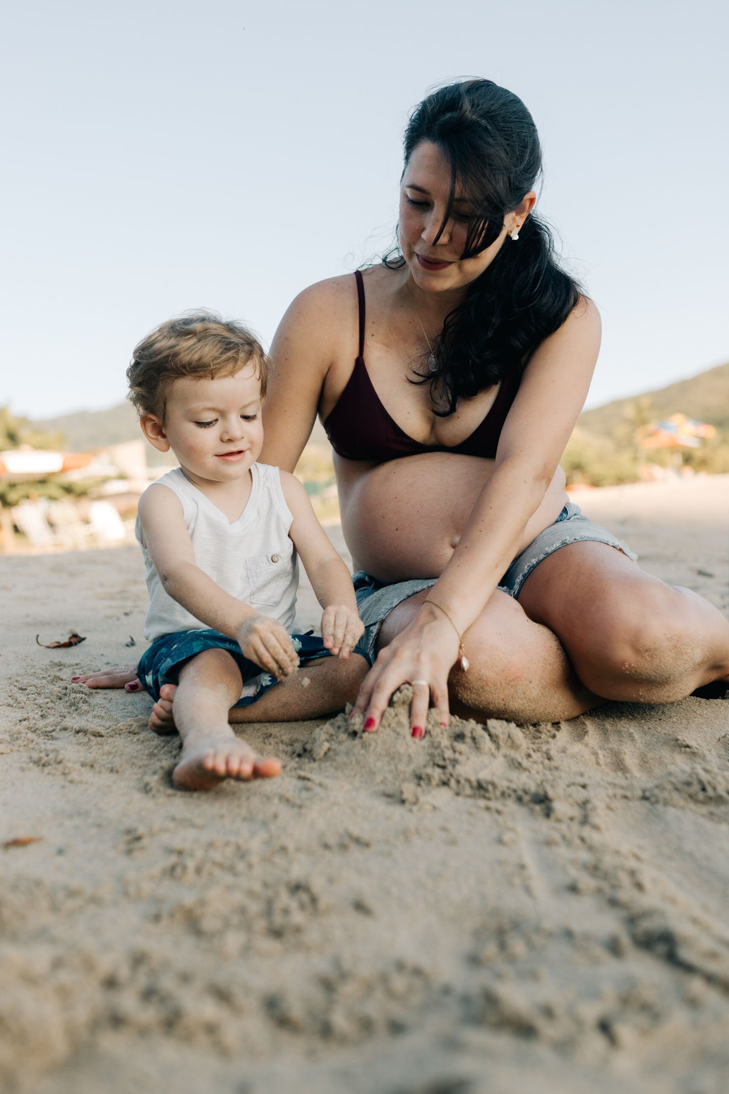 A toddler and adult play together in the sand on a sunny beach, enjoying quality time together.