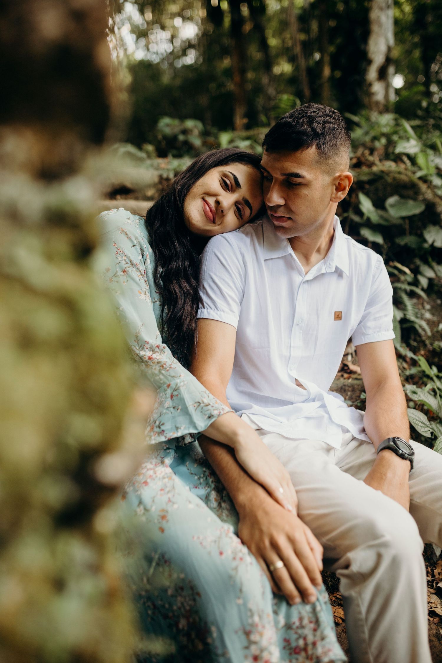 Intimate outdoor portrait of couple in coordinating outfits amid natural greenery.