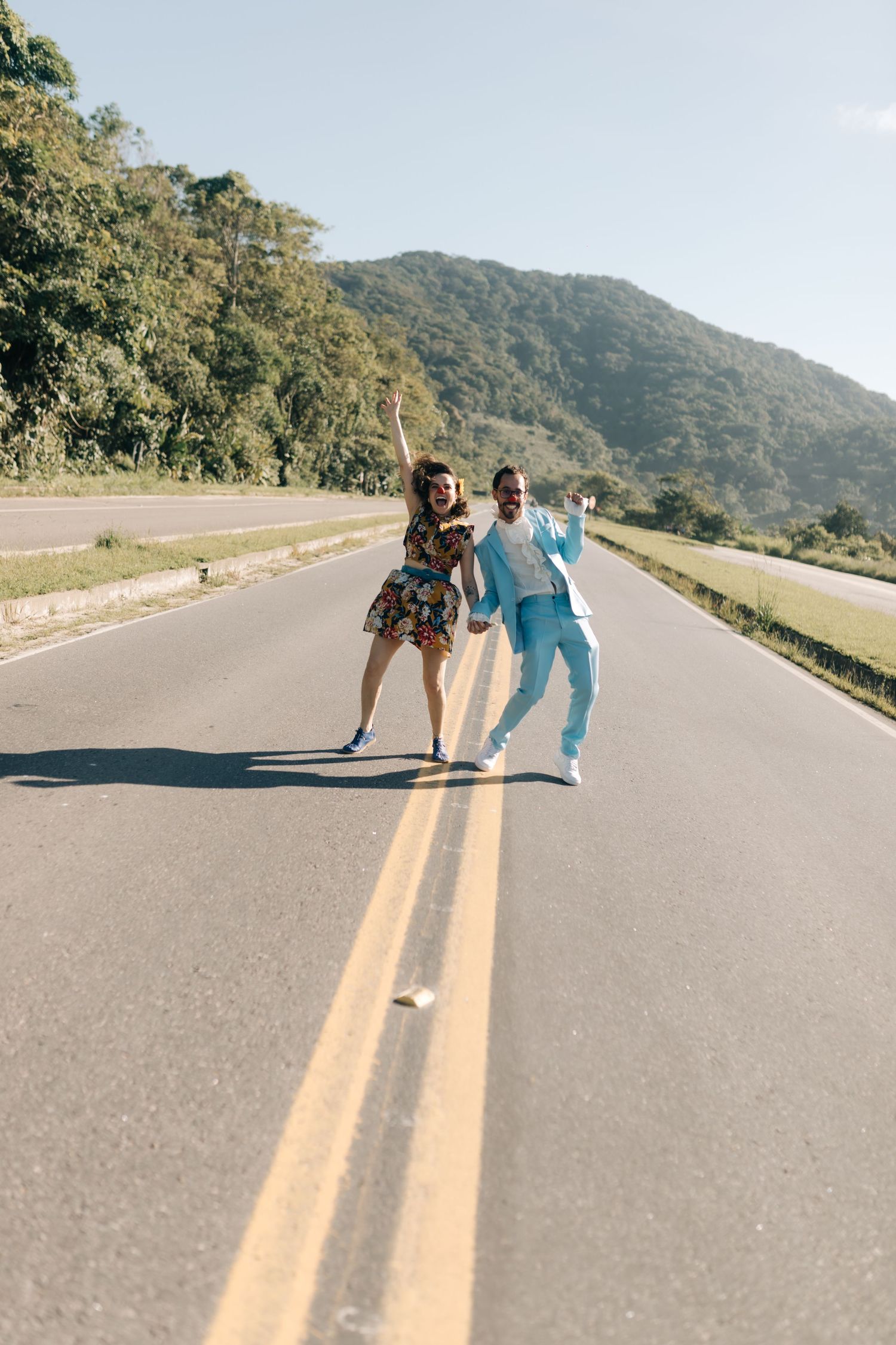 Two people dancing playfully on a mountain road with lush green hills in the background.