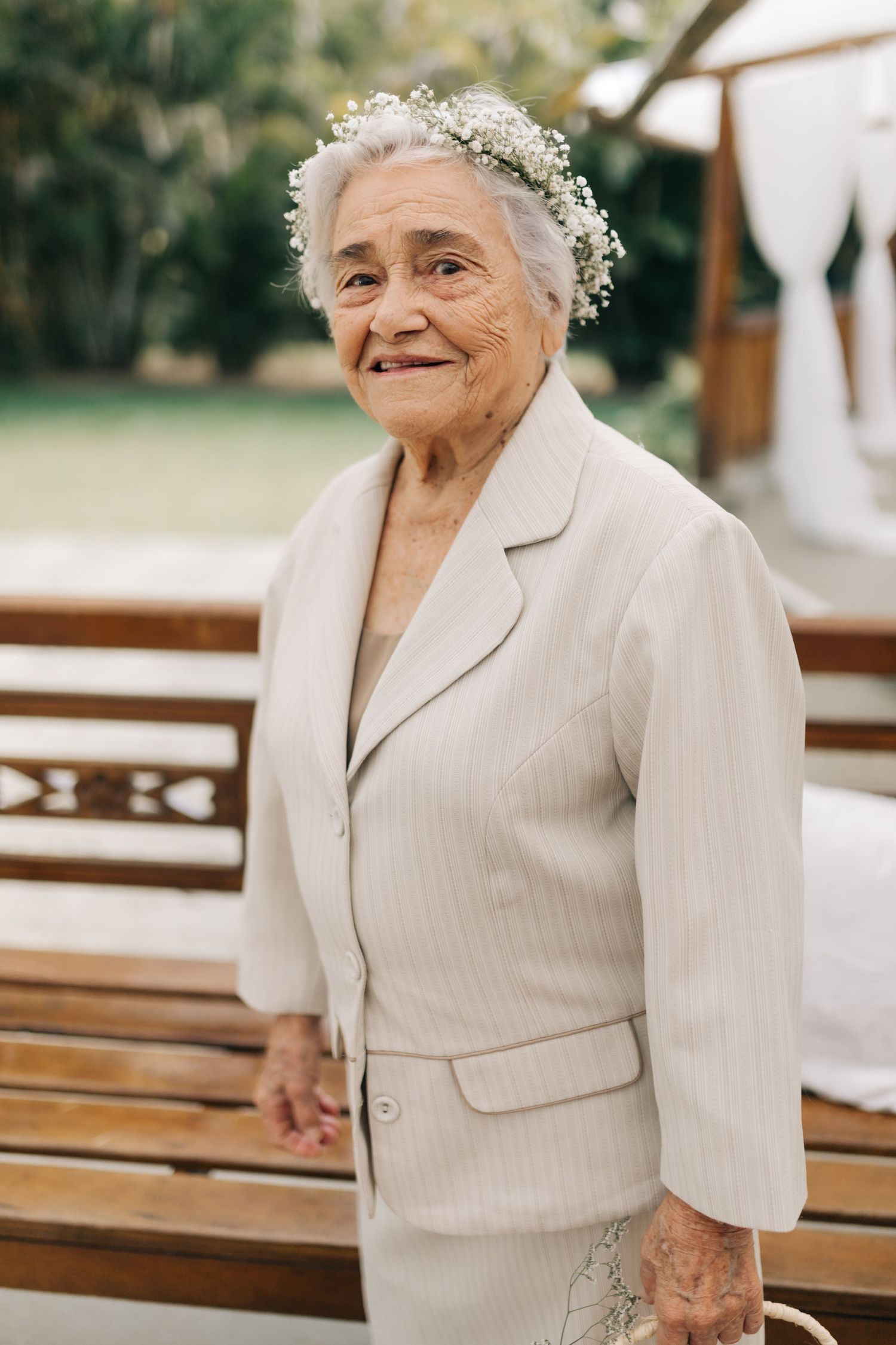 Wedding guest in cream suit and floral crown smiling outdoors.