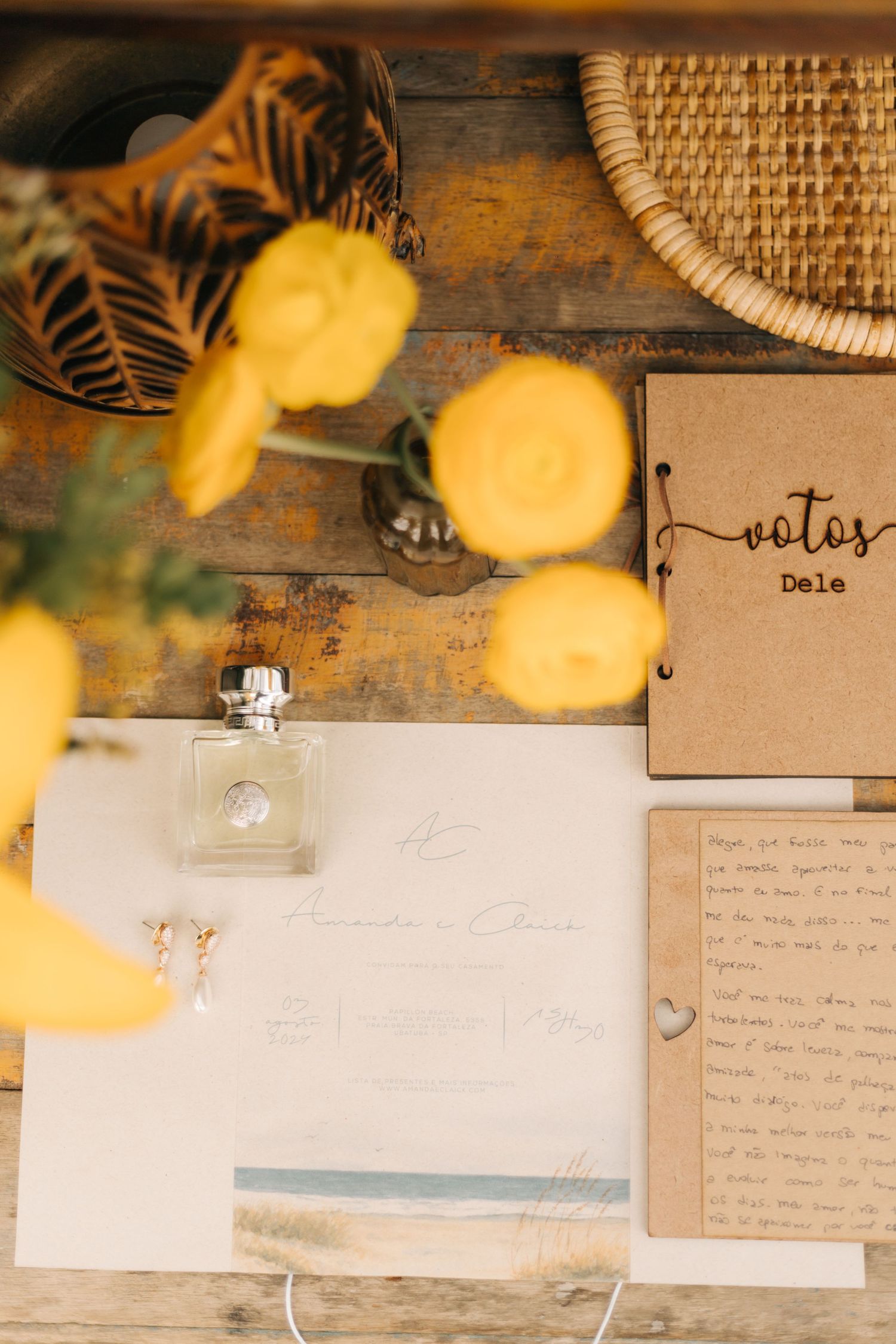 Wedding details flatlay with notes and perfume bottle accented by blurred yellow flowers.