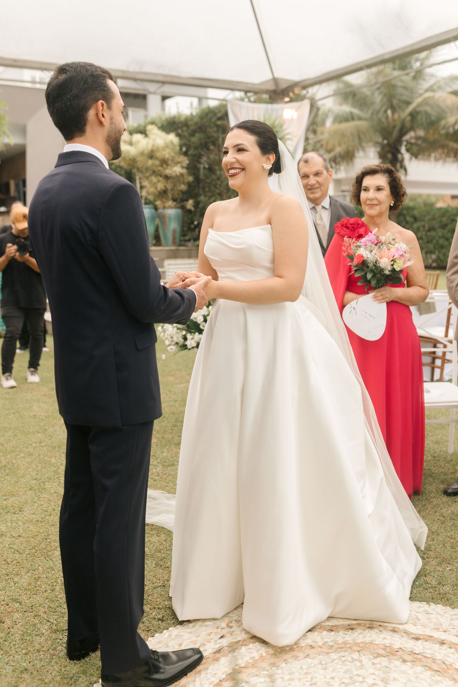 An outdoor wedding ceremony with guests watching as couple exchanges vows on a decorated lawn.