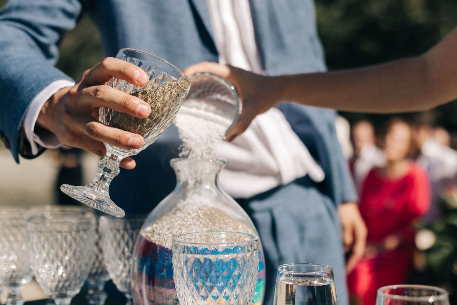 Hands pouring sand into an elegant glass vessel during a ceremony.