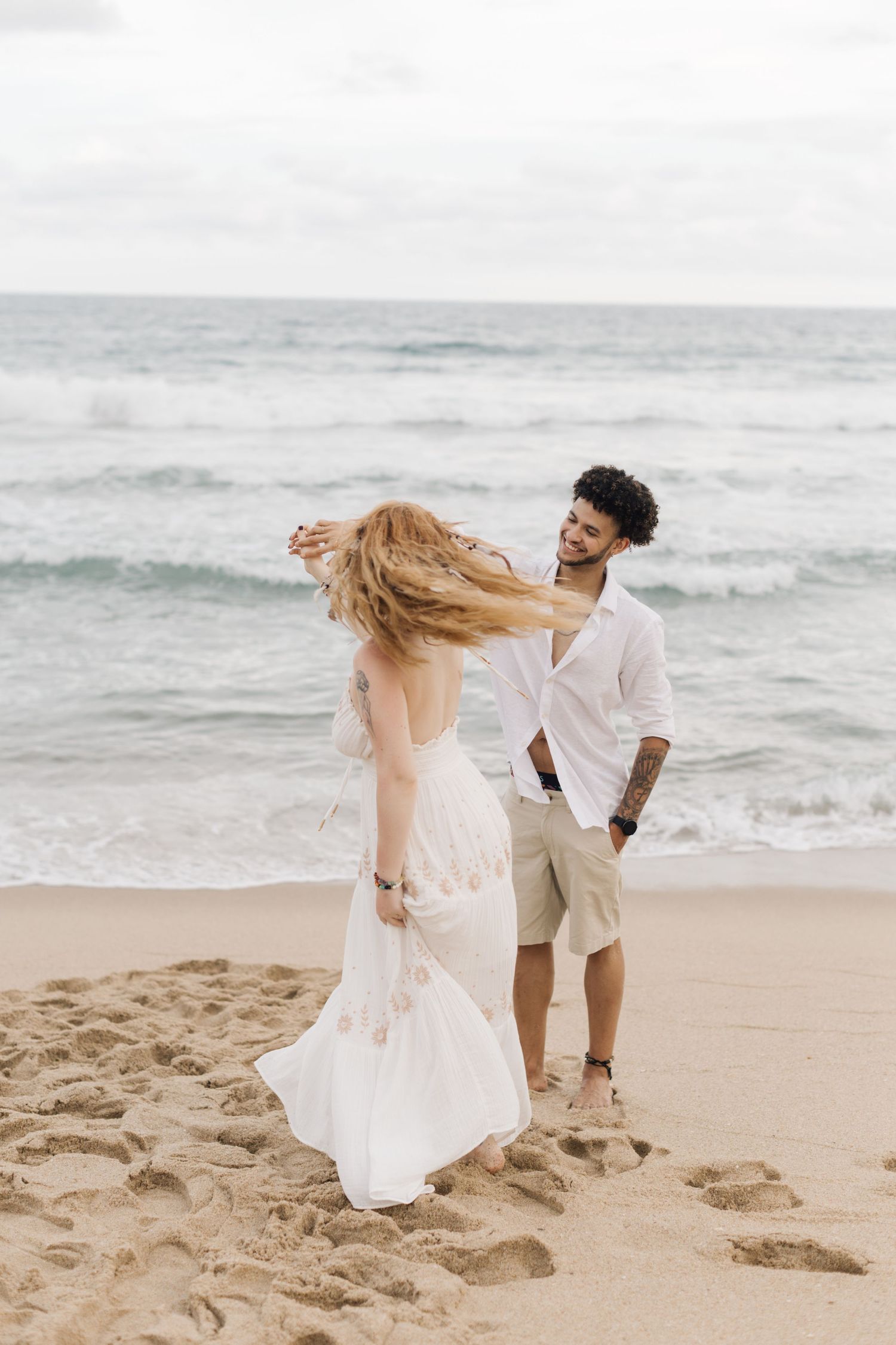 A romantic couple dances together on a sandy beach with waves and ocean in the background.