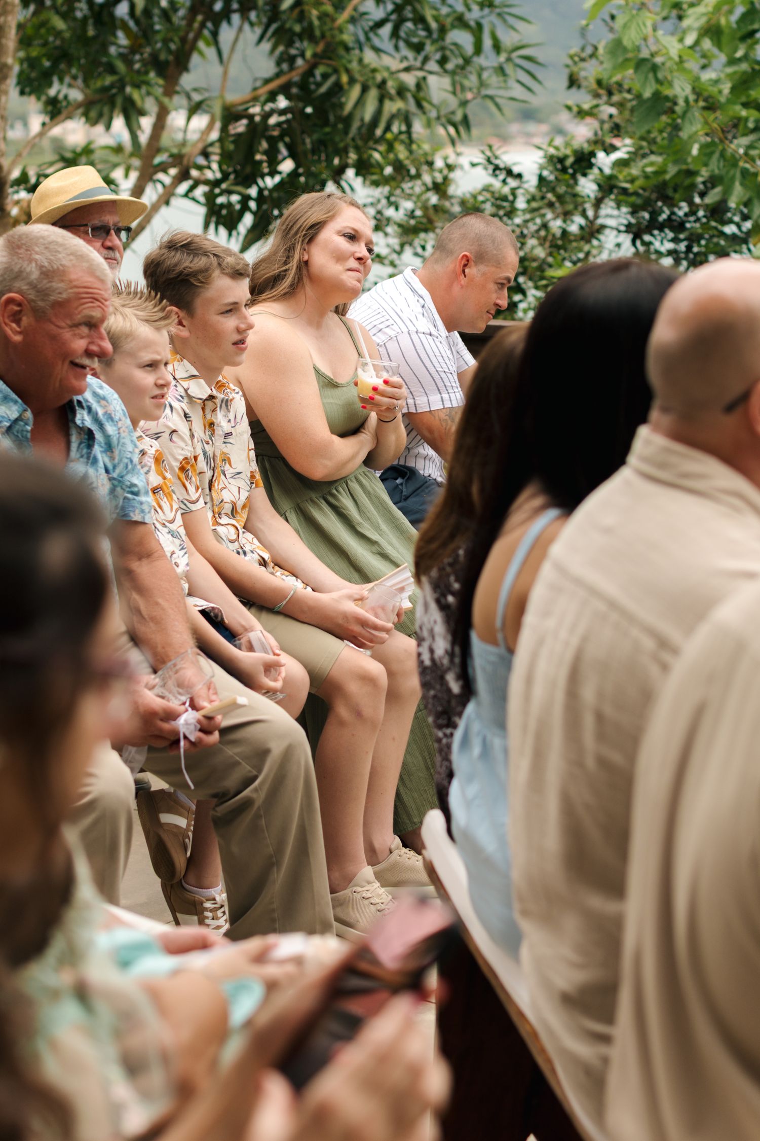 Wedding guests seated outdoors watching ceremony in casual summer attire.