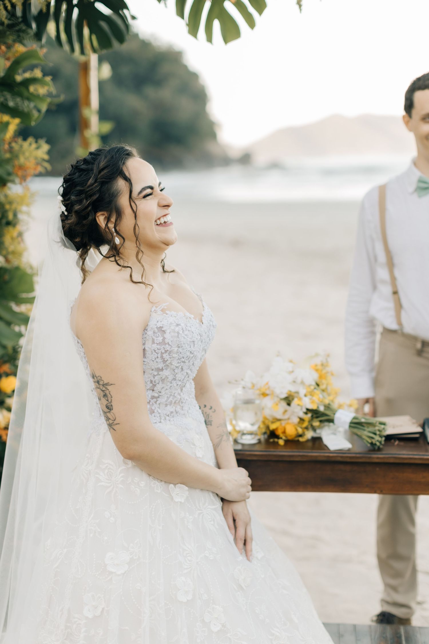 Joyful bride laughs while reading wedding vows at beach ceremony.