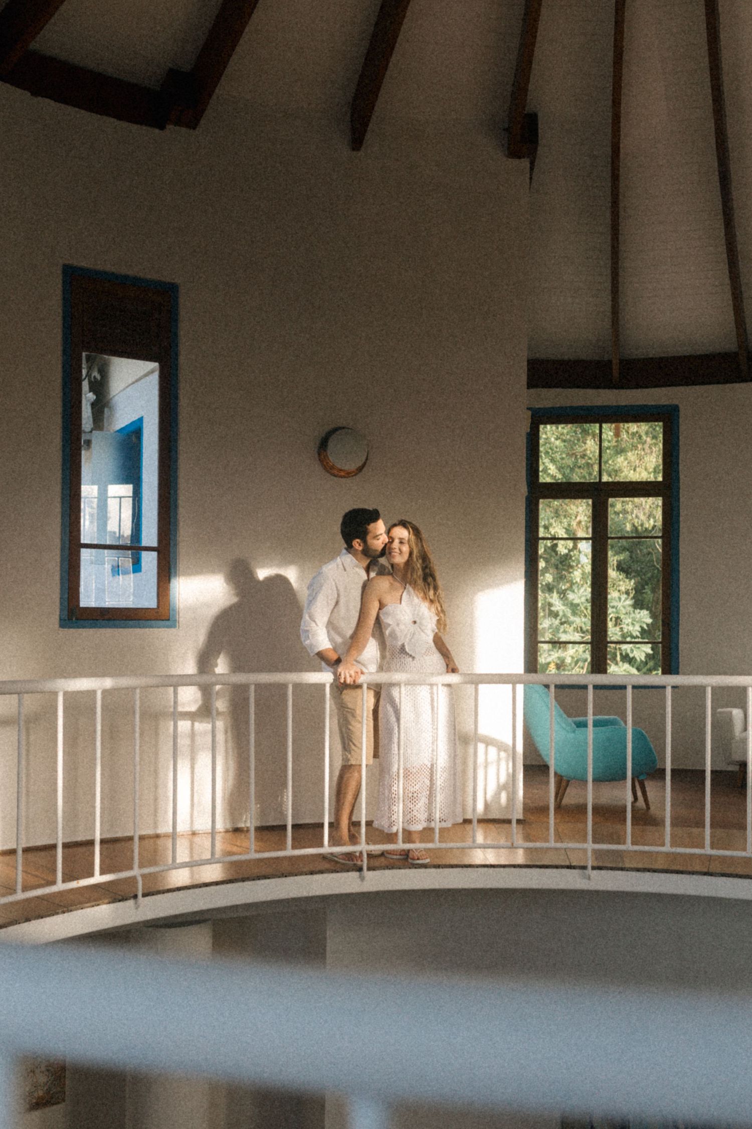 A romantic moment captured on a curved indoor balcony with dramatic shadows and natural lighting.