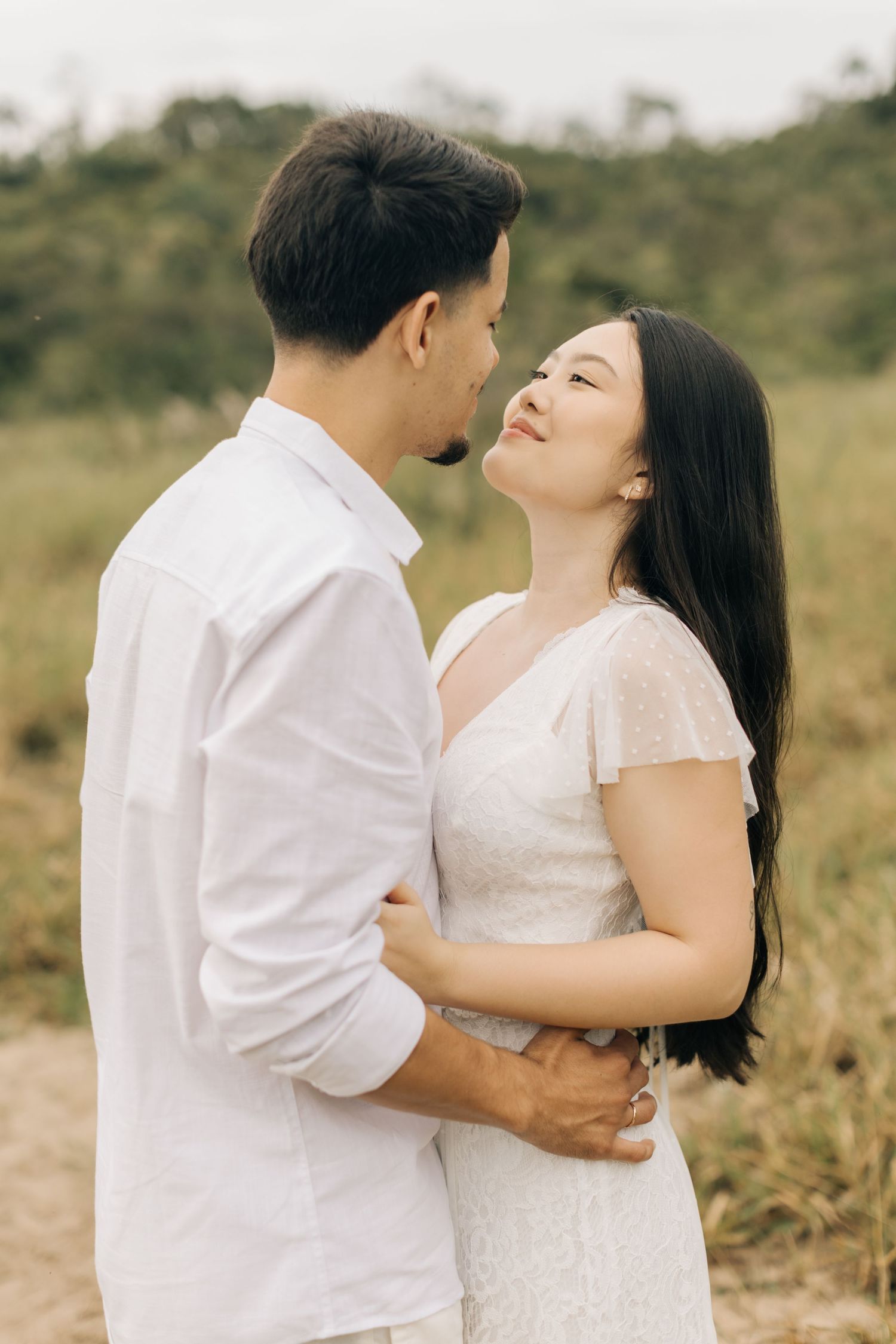 A romantic couple embraces in a natural outdoor setting wearing coordinated white outfits.