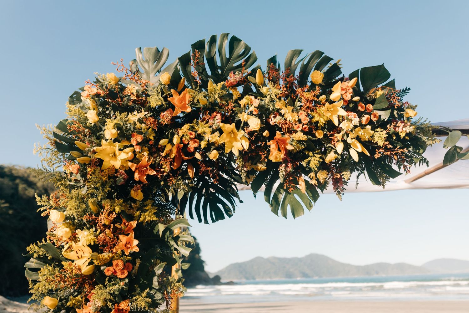 Tropical floral arch with orange and yellow blooms against beach backdrop.