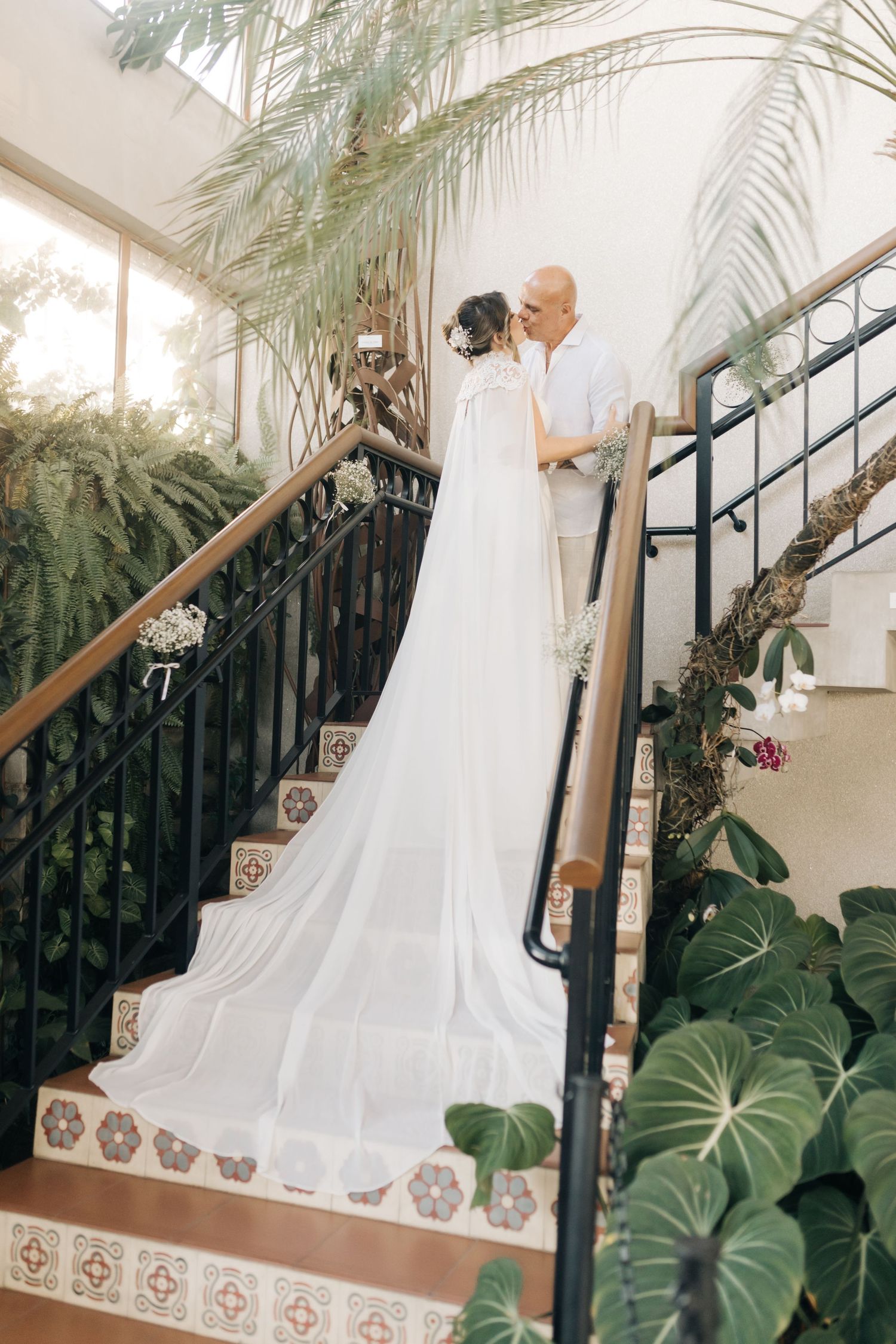 A couple descends an elegant staircase adorned with tropical plants and palm fronds.