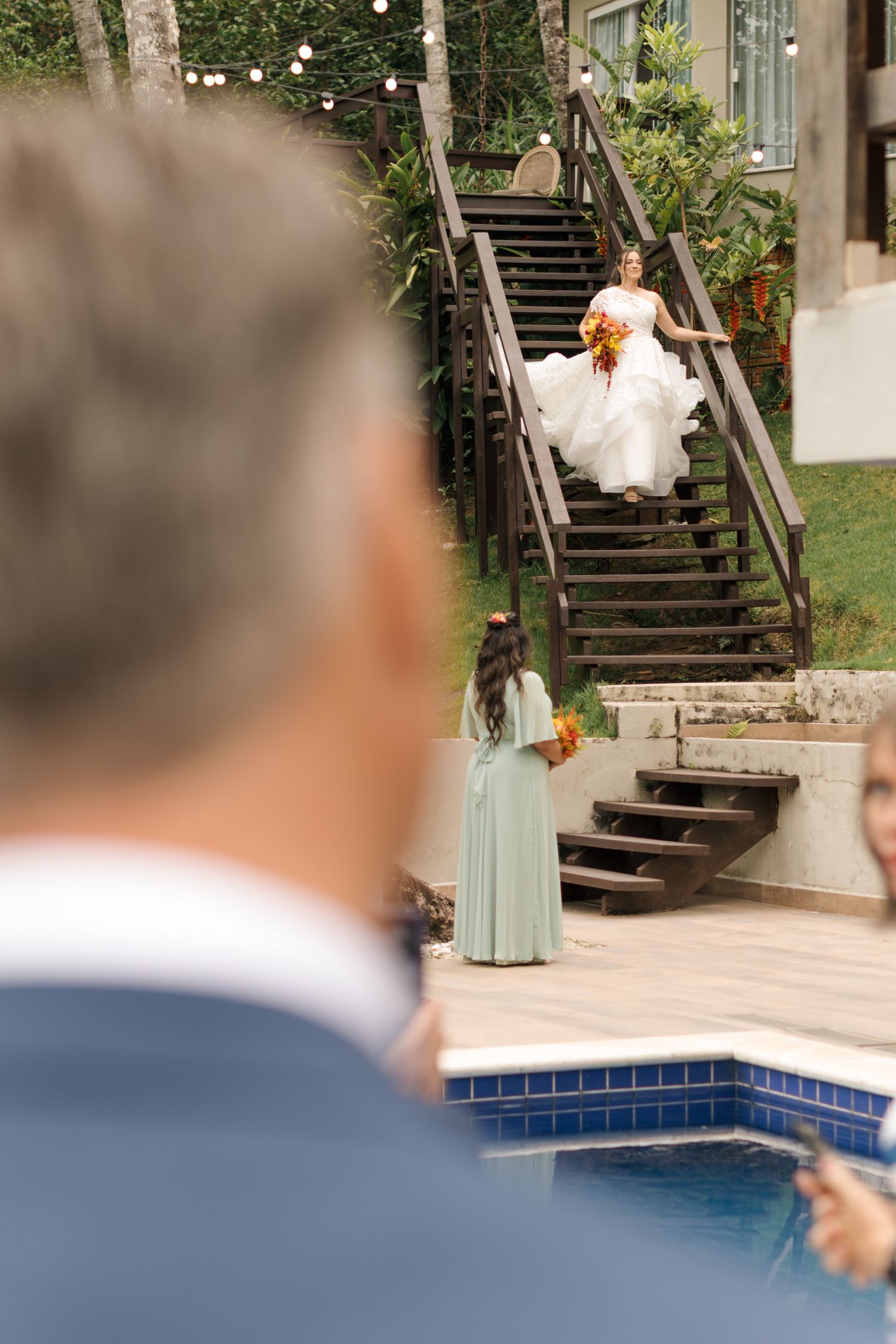 Elegant outdoor wedding venue with wooden stairs and a swimming pool surrounded by lush greenery.