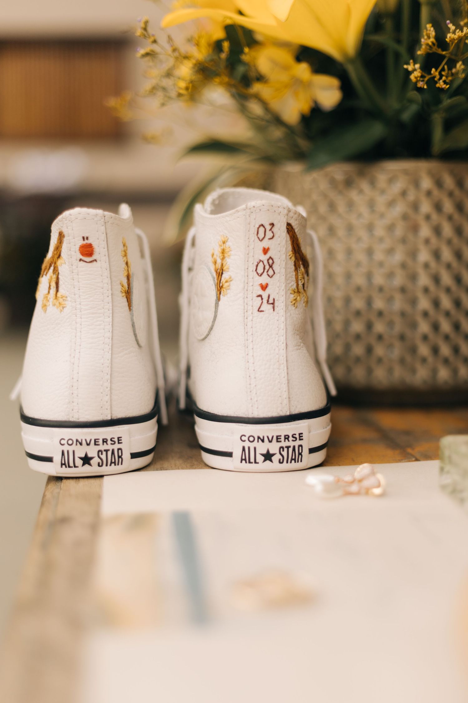 White Converse All-Star sneakers with custom floral details and a date displayed next to yellow flowers.