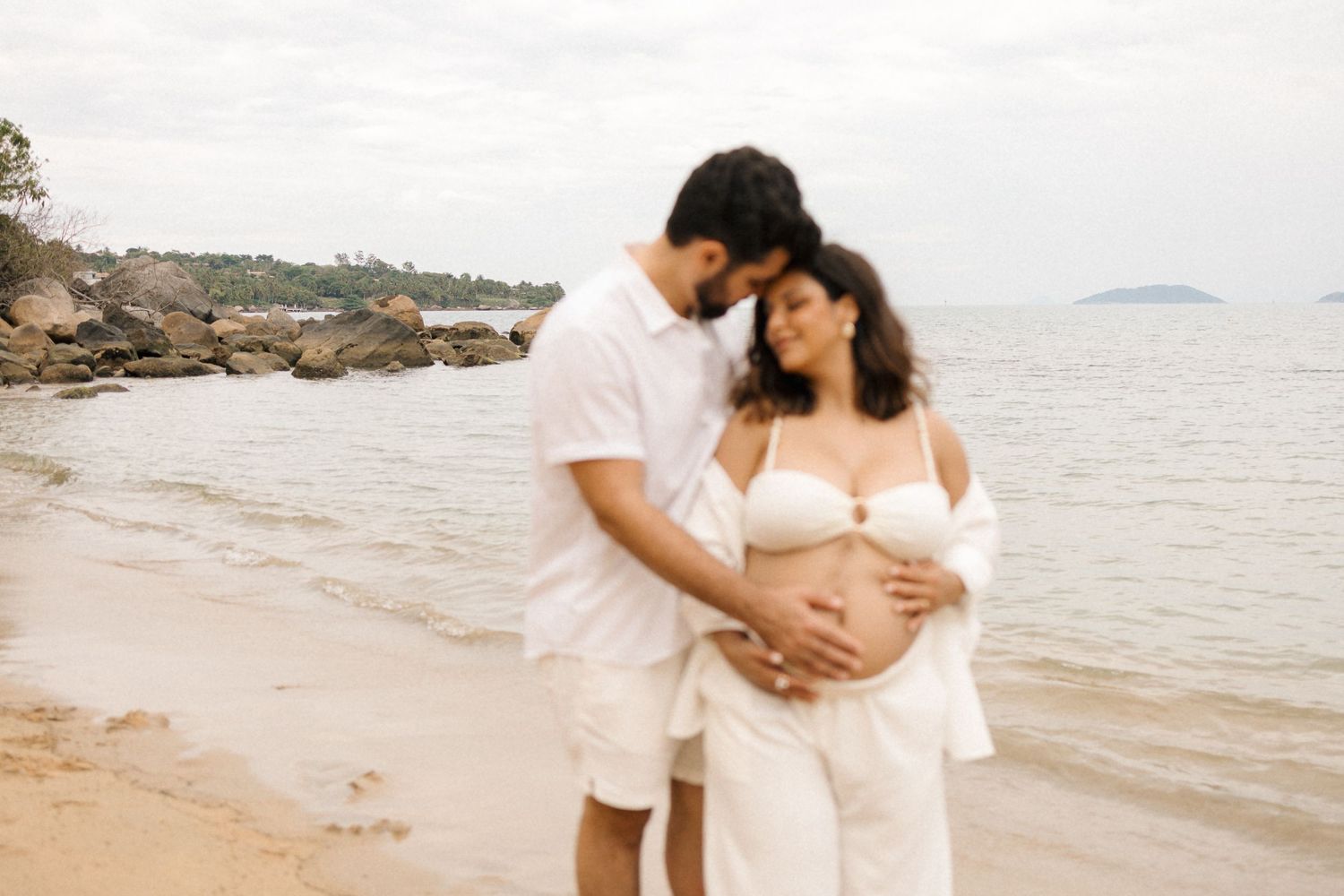 A couple embraces on a serene beach during a romantic photoshoot at sunset.