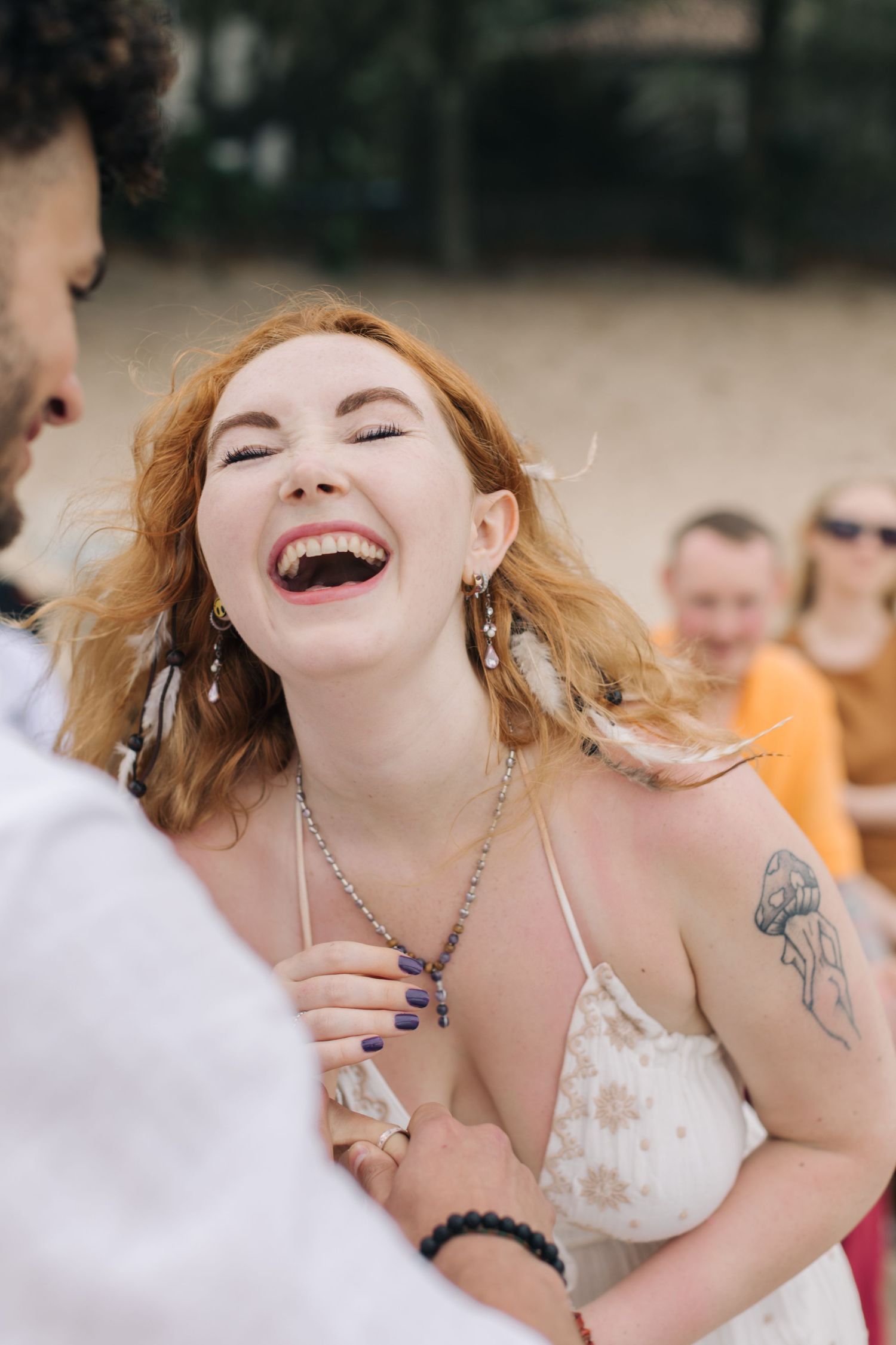 Candid laughter during seaside wedding ceremony with guests in background.