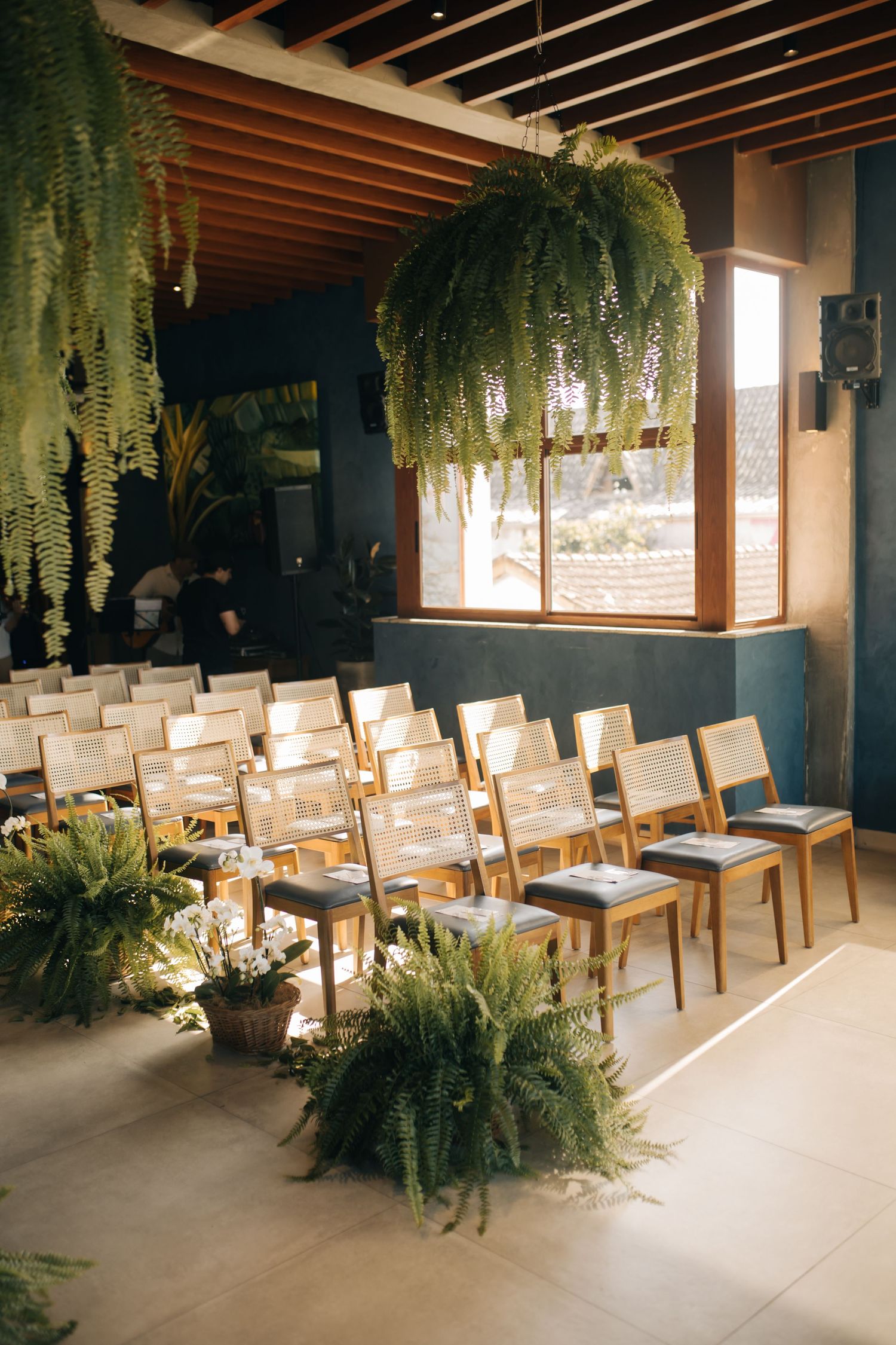 Wedding ceremony space with rows of wooden chairs and dramatic hanging ferns from wooden beams.