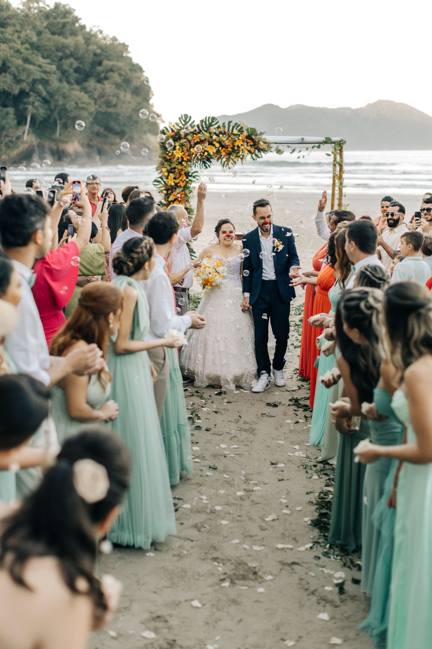 Beachside wedding celebration with guests in mint dresses and floral arch backdrop.
