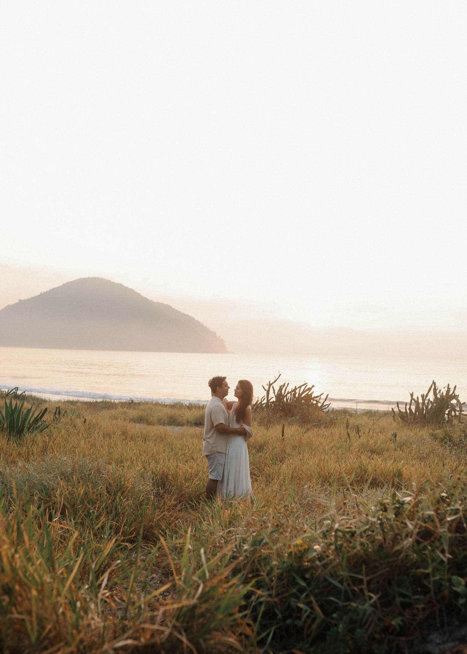 Silhouettes of a couple walking through coastal grasslands at sunset with mountains in view.