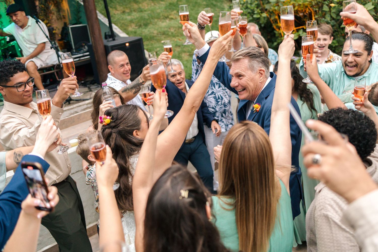 Wedding guests raising glasses in celebratory toast during outdoor reception.
