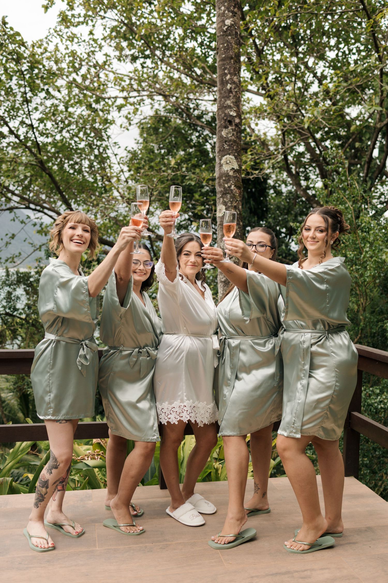 Wedding party in matching silver robes poses playfully on an outdoor terrace.