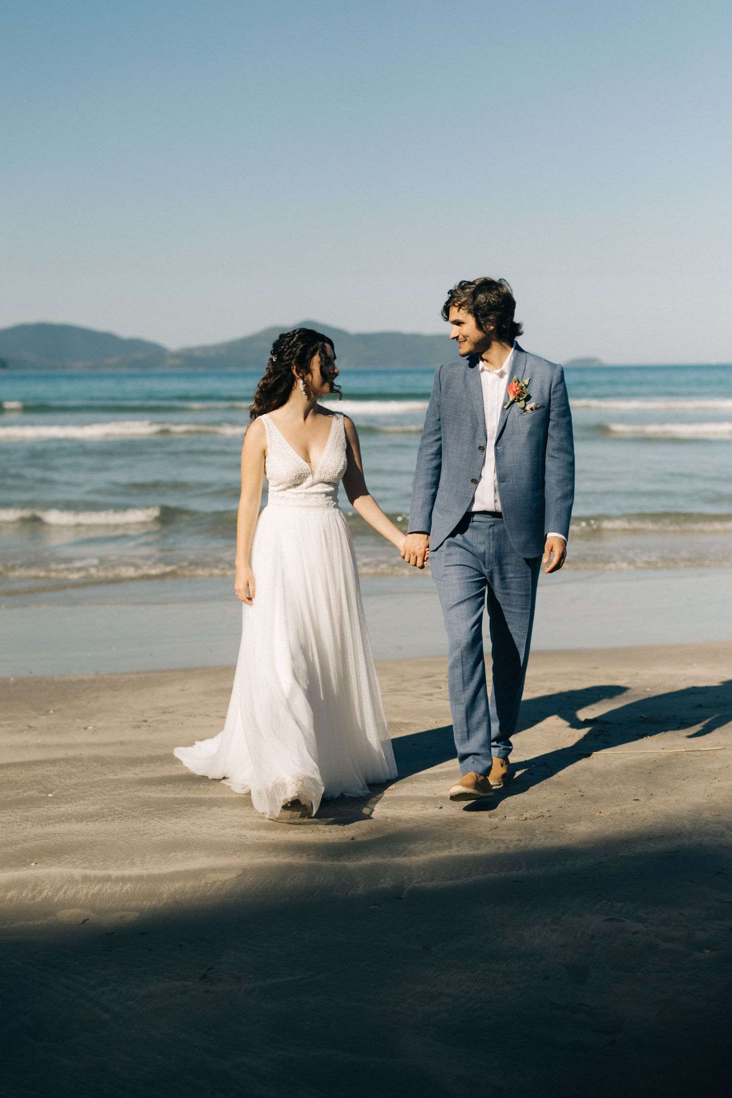 Couple walking hand in hand on a scenic beach in wedding attire.