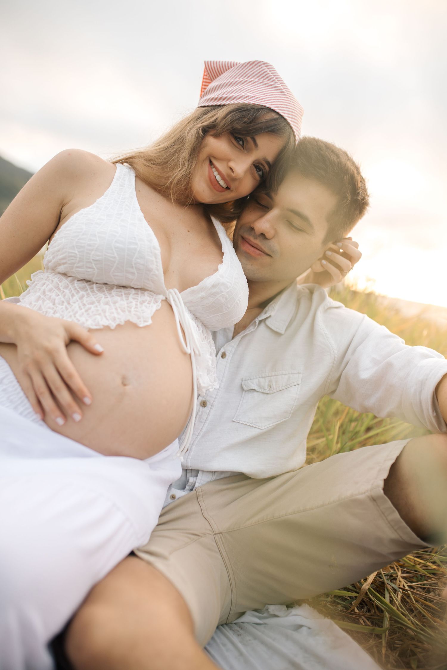 Intimate maternity photo of couple embracing in a sunlit field at golden hour.