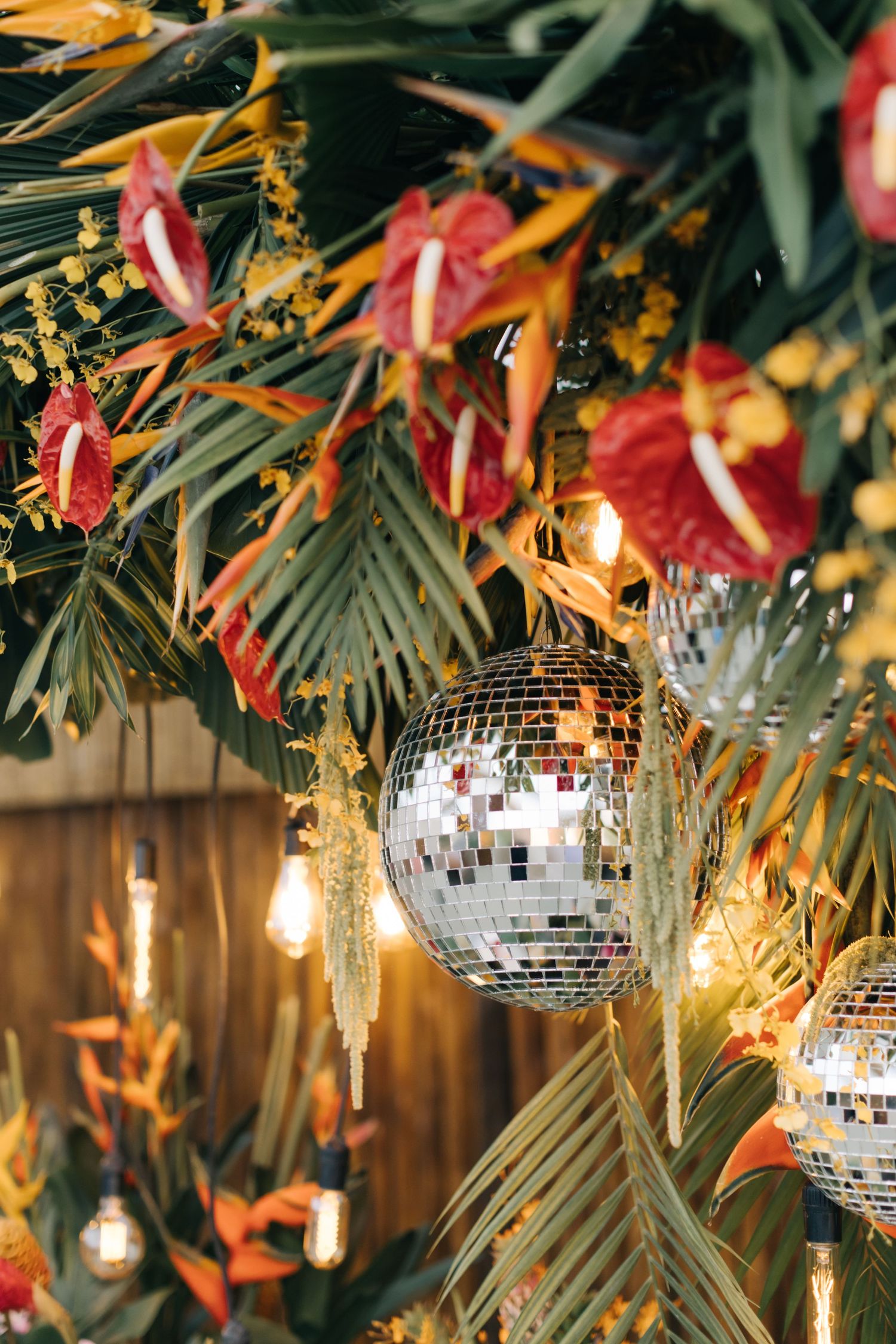 Tropical party decor featuring mirror balls, string lights, and colorful floral arrangements.