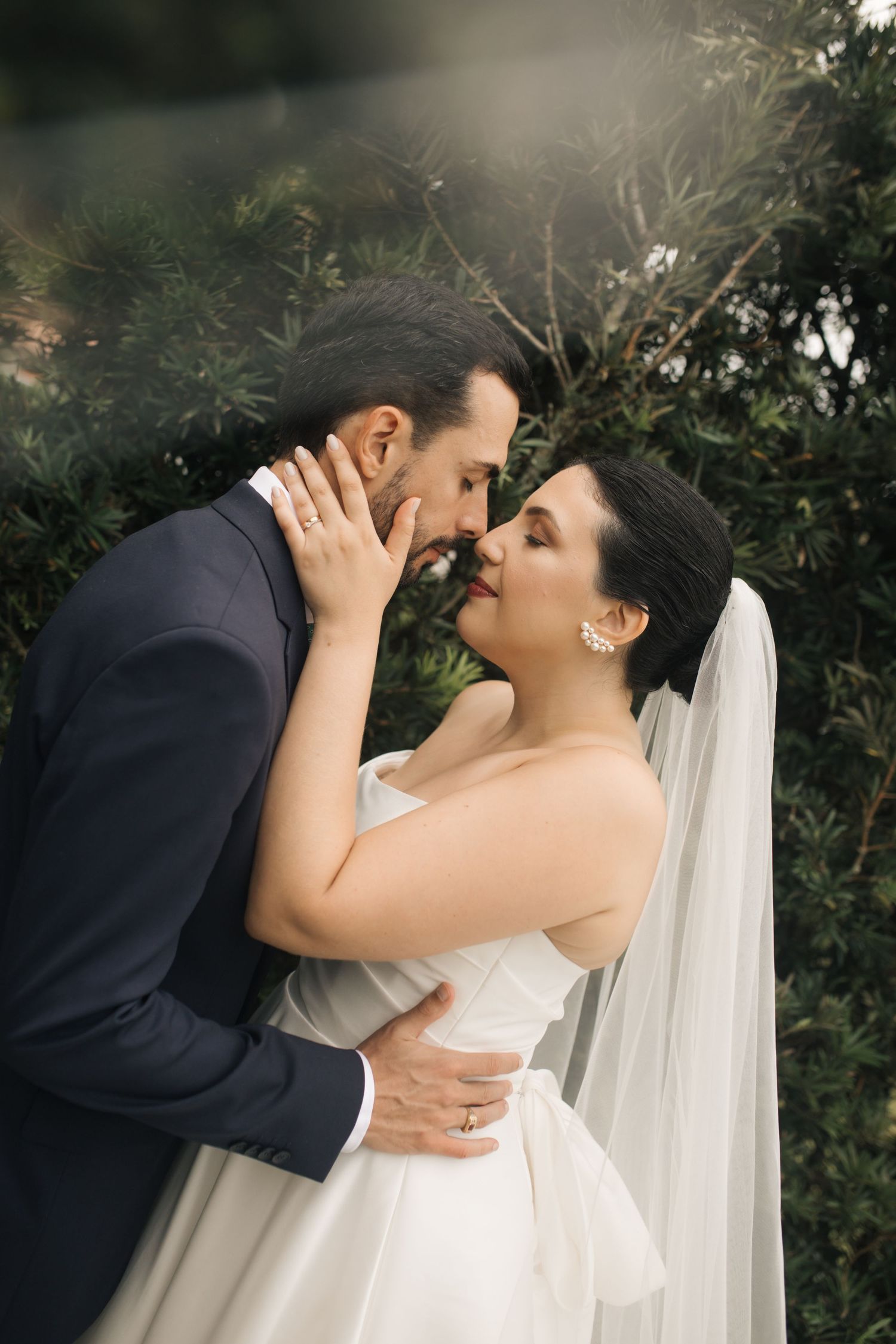 An intimate wedding portrait shows a tender moment between newlyweds against a garden backdrop.