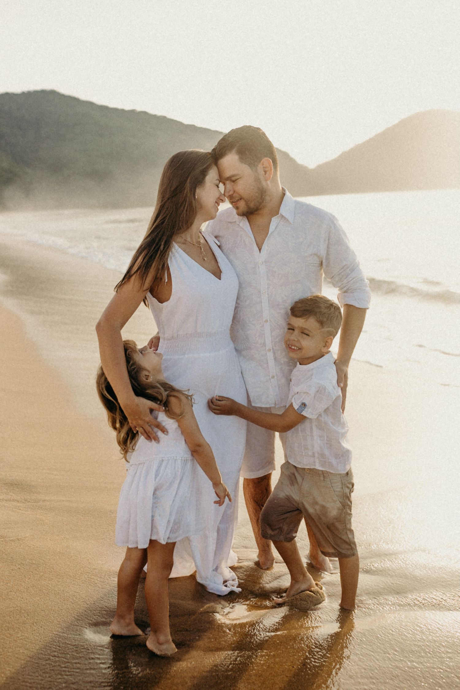 Family wearing white outfits enjoys quality time together on a scenic beach at sunset.
