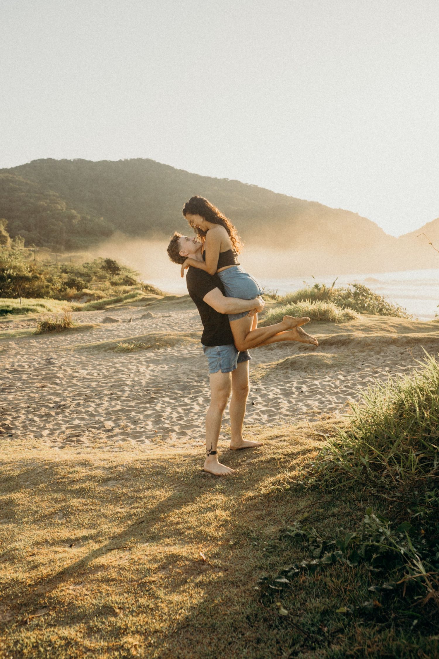 Couple sharing a joyful moment on coastal clifftop during sunset.