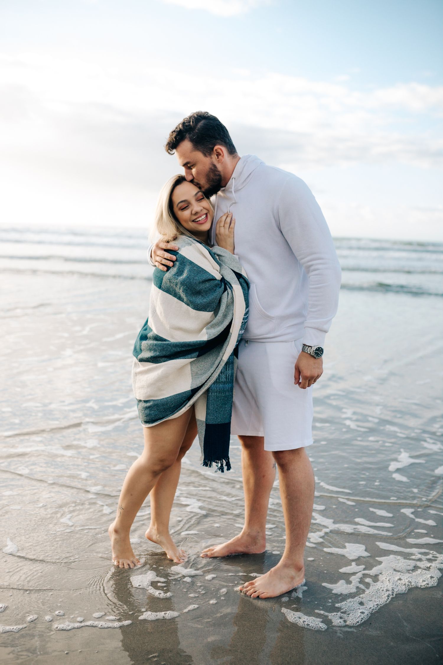 Tender embrace between couple standing in ocean waves during beach photoshoot.
