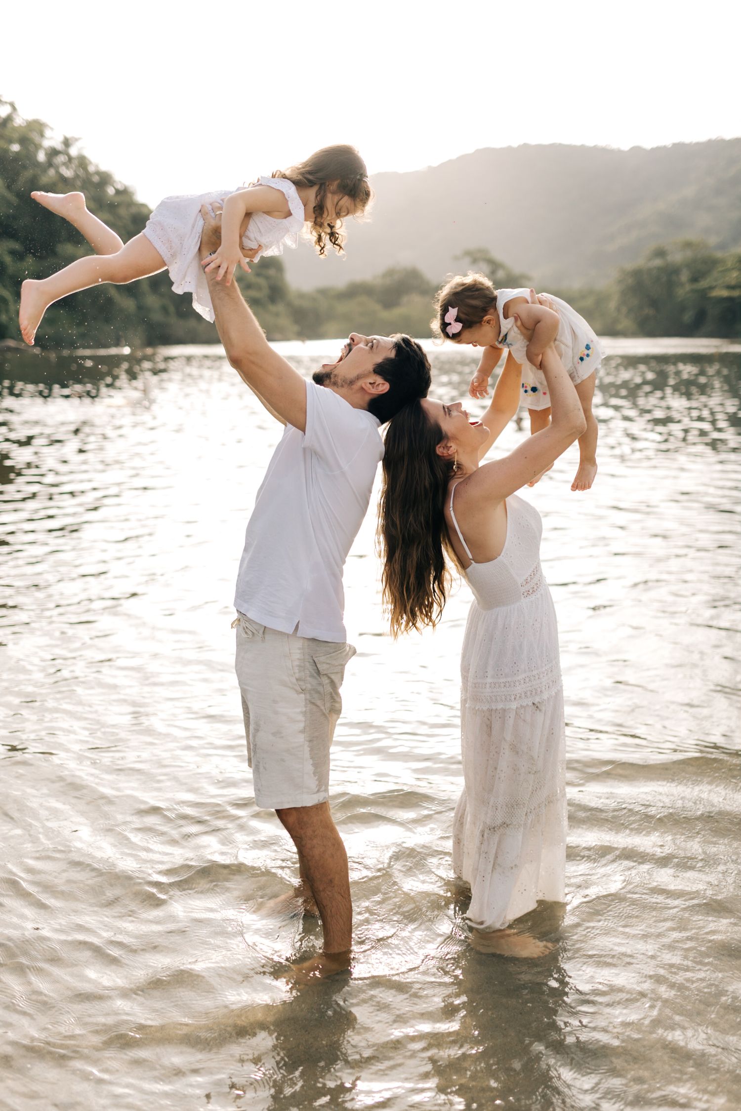 Family enjoying playful moments in ocean water during sunset at a tropical beach.