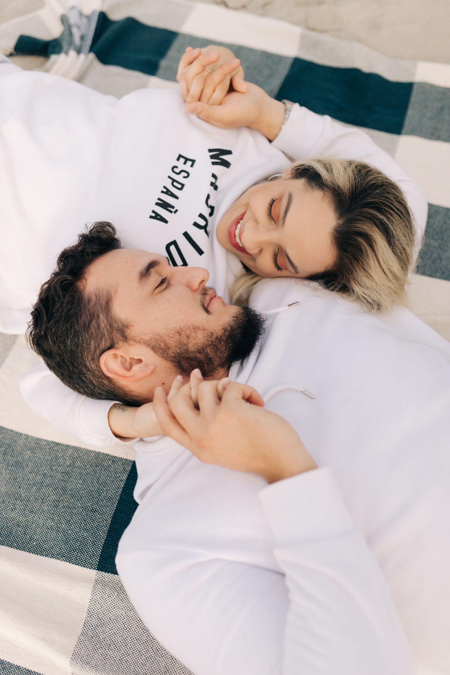 Couple laughing together while relaxing on a gray and white striped blanket.
