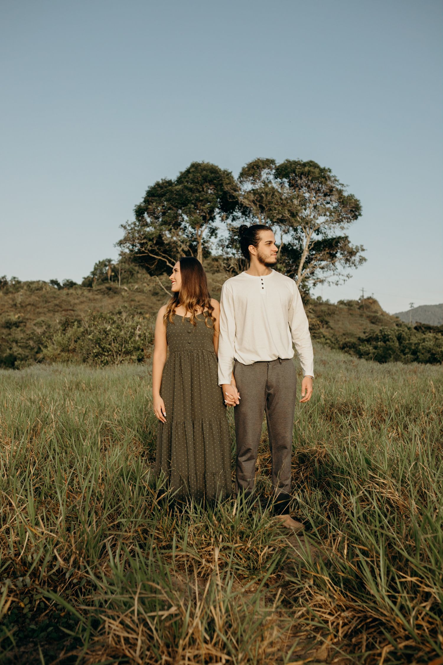 A couple stands in a scenic field with eucalyptus trees during golden hour.