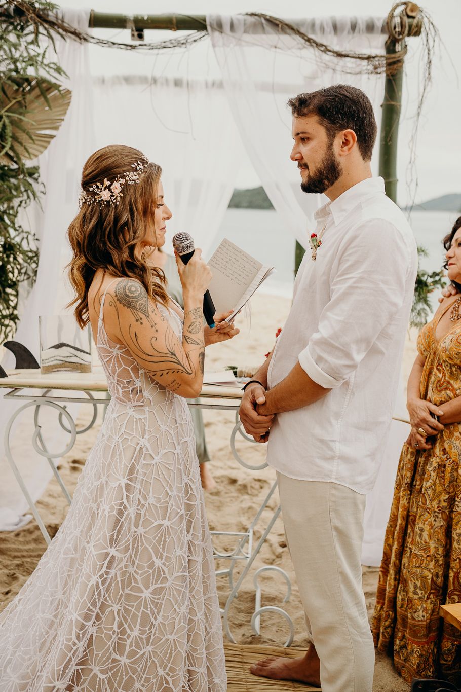Couple exchanging vows during intimate beach wedding ceremony with white fabric backdrop.