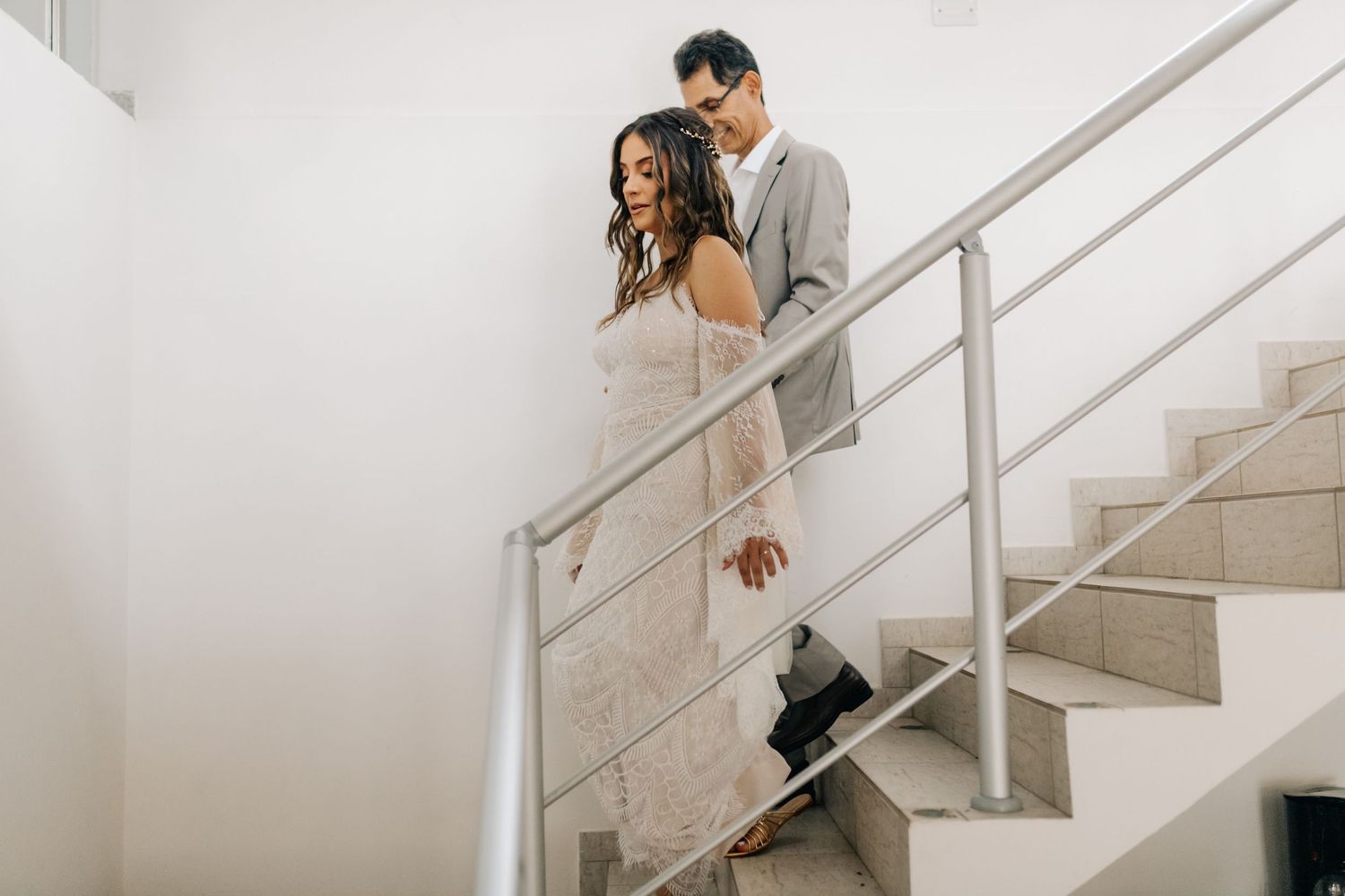A couple descending a modern white staircase during their wedding day.