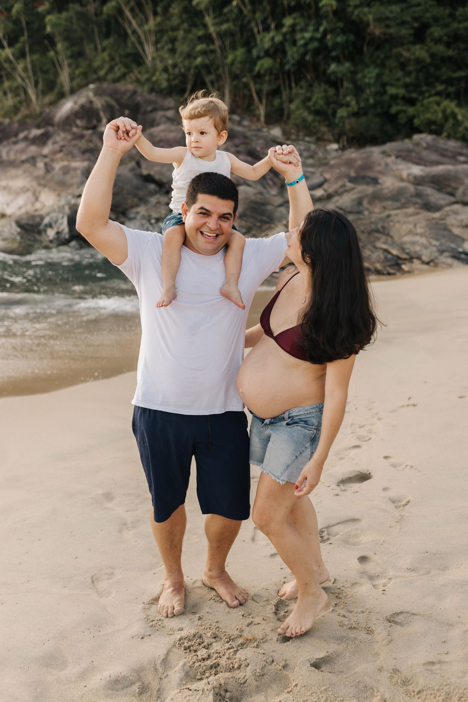 Casual beach photoshoot capturing spontaneous family moments near rocky shoreline.