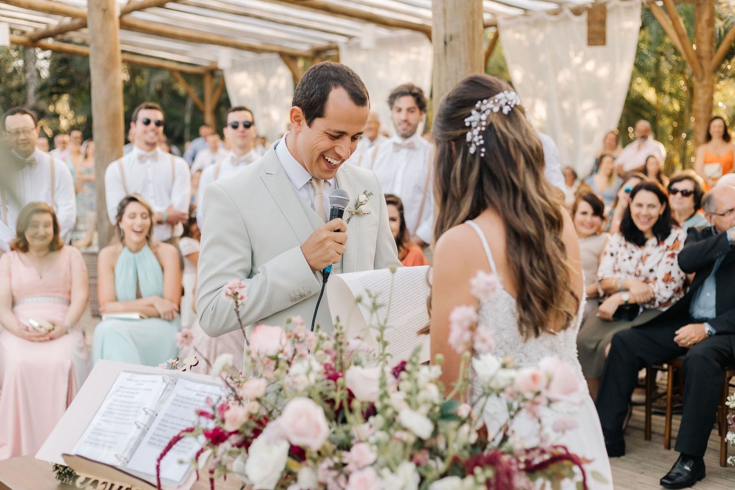 Wedding celebration with guests seated beneath wooden beams and floral arrangements.