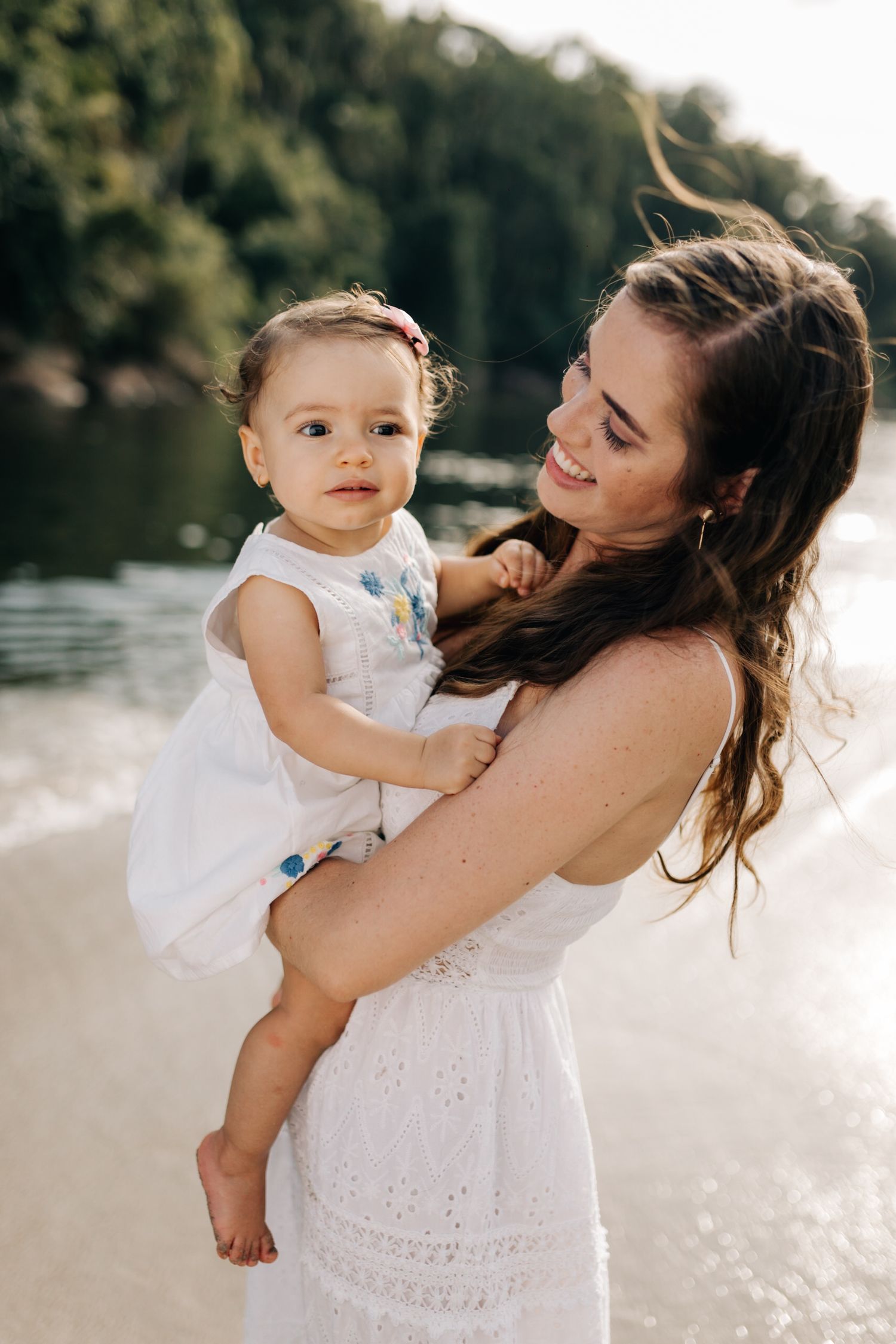 Sweet interaction between adult and toddler wearing matching white outfits near water.