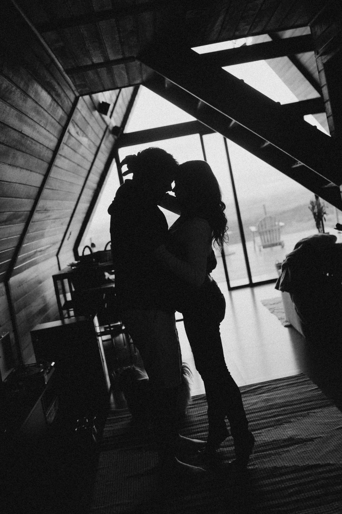 A silhouetted couple shares a tender moment in a rustic wooden interior with dramatic lighting.