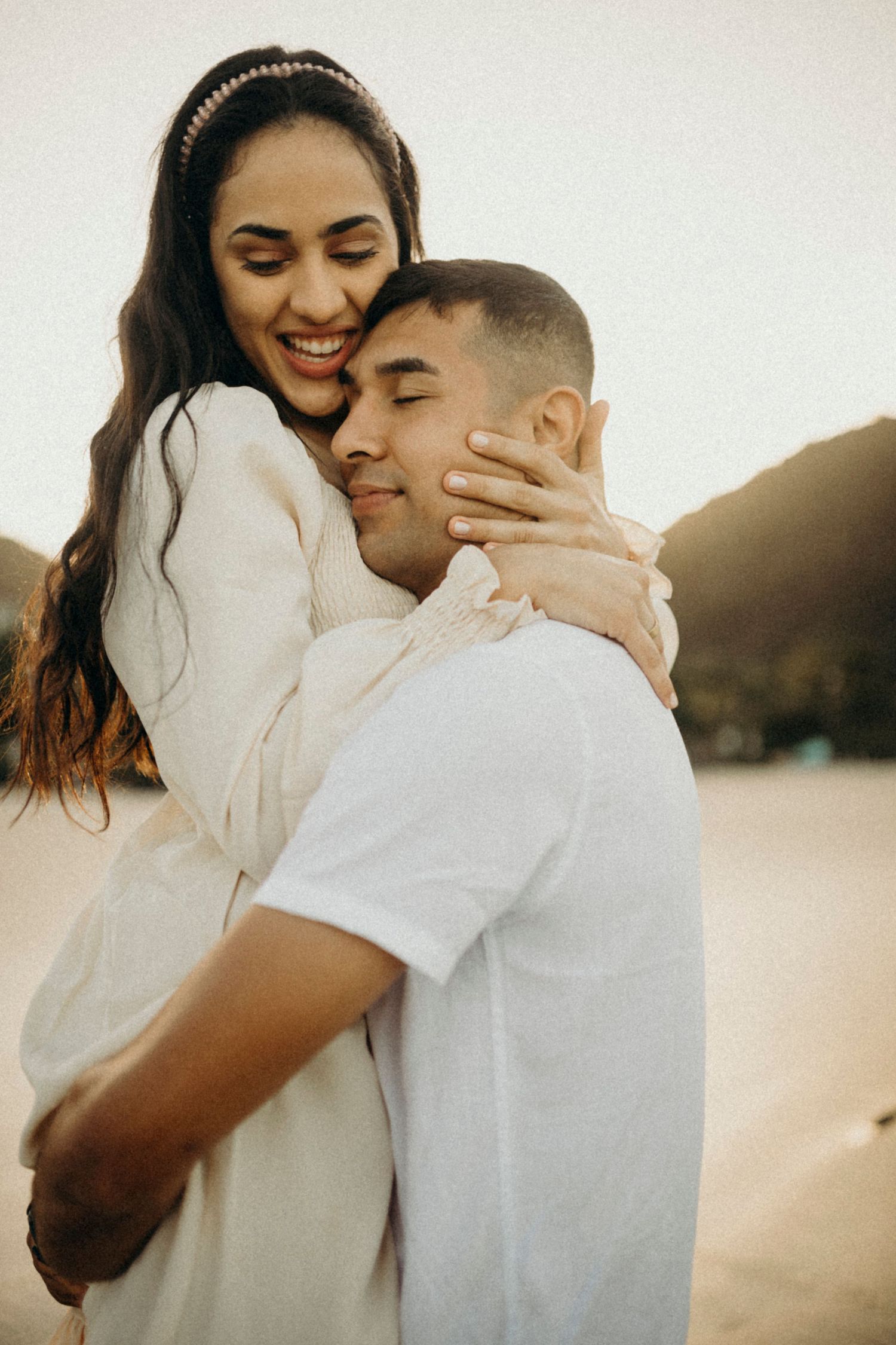 Couple shares intimate embrace while laughing together on beach.