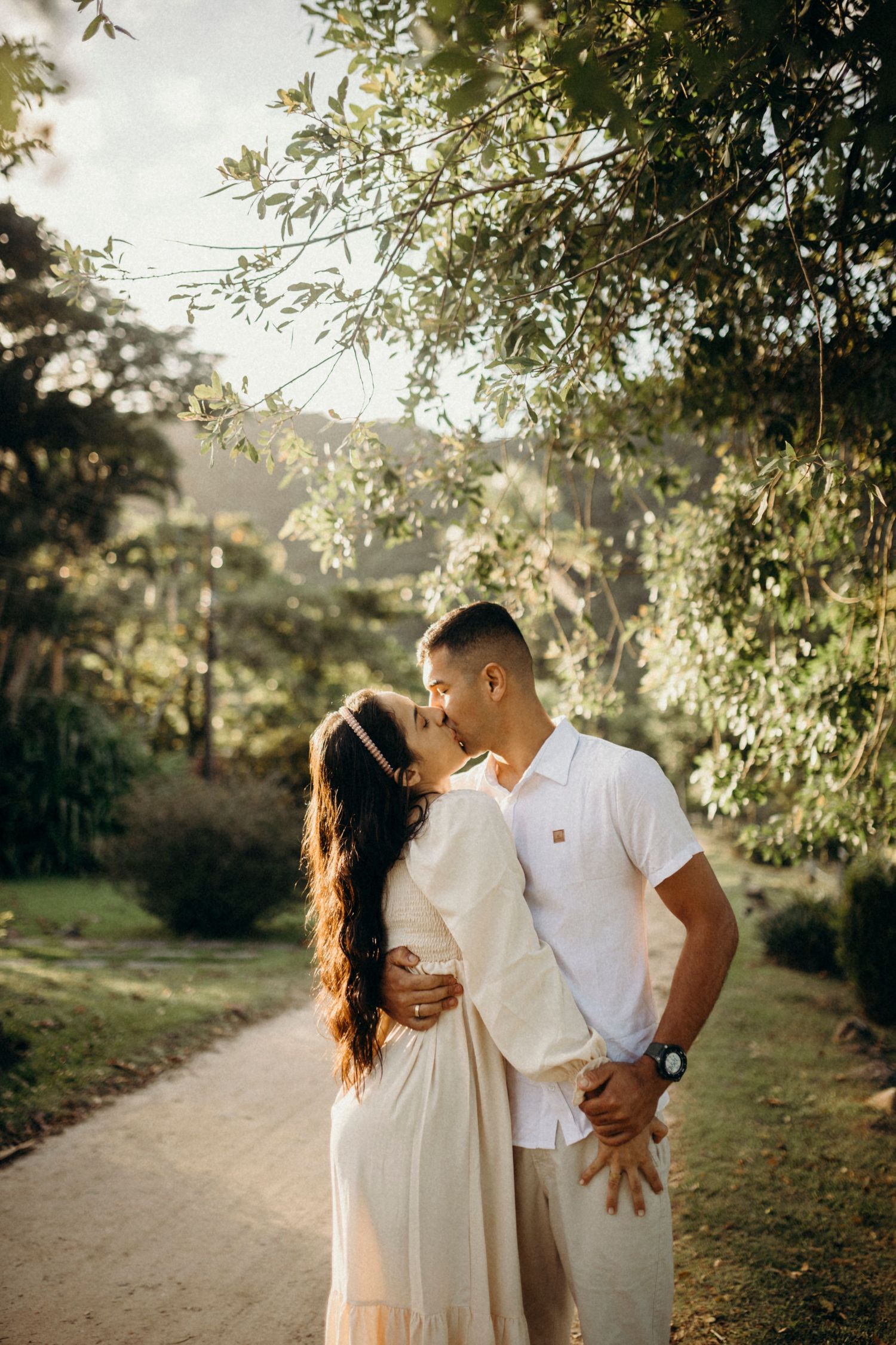 A romantic couple shares an intimate moment on a tree-lined path in warm afternoon light.