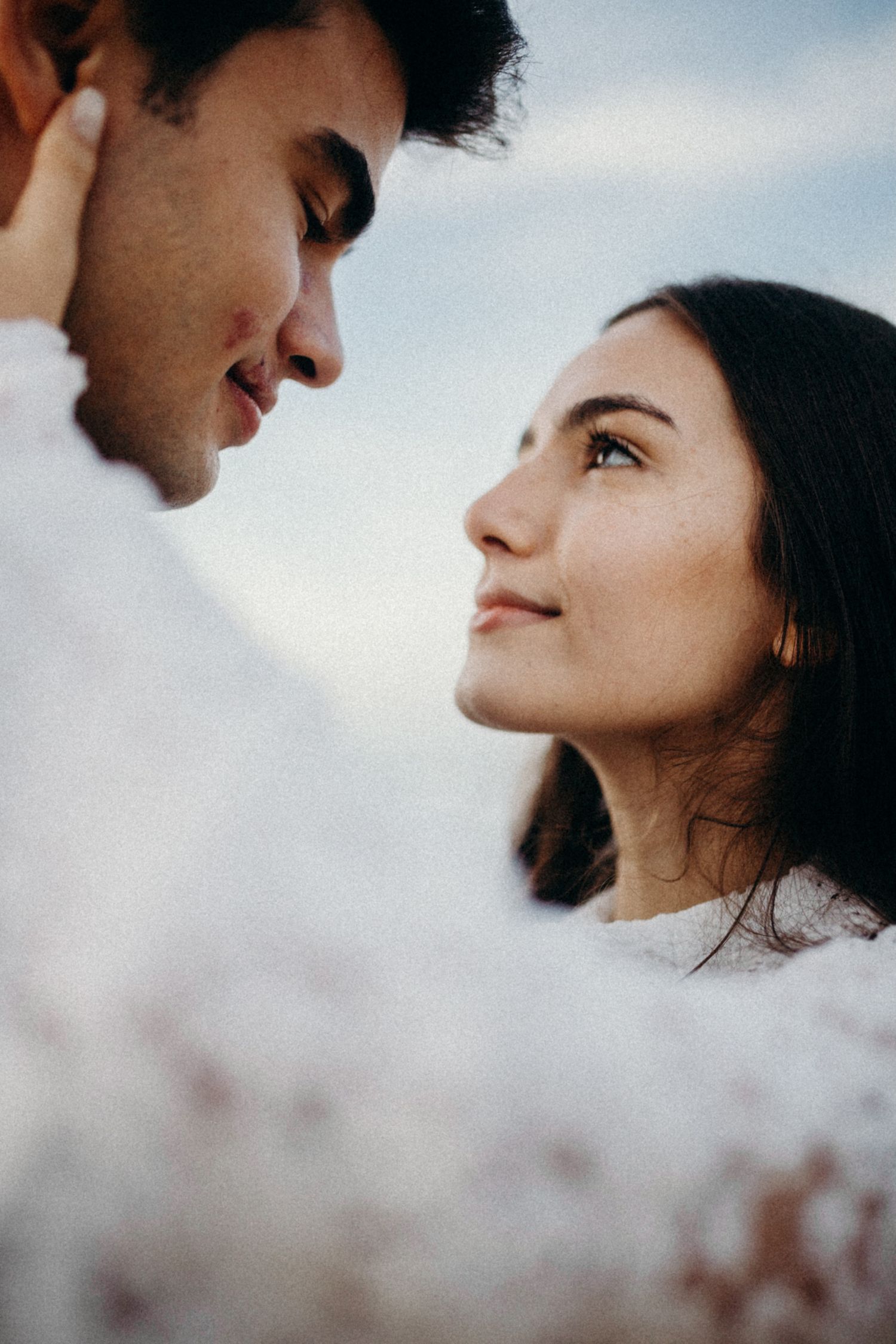 Close-up intimate portrait of a couple gazing at each other against a soft sky background.