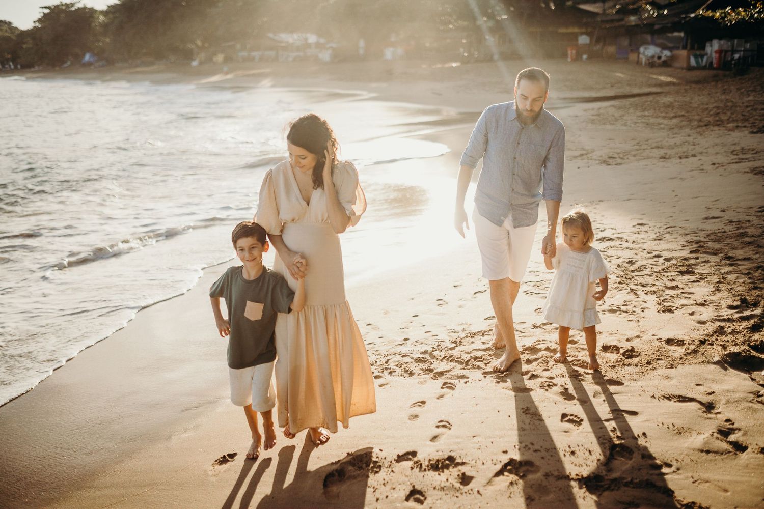 A family takes a sunset stroll along a sandy beach with long shadows cast on the shore.
