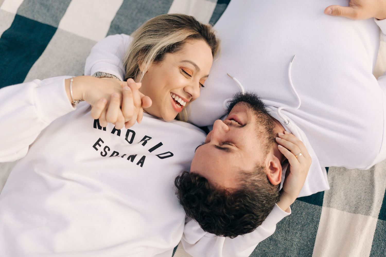 Couple lying on checkered blanket wearing matching white shirts.