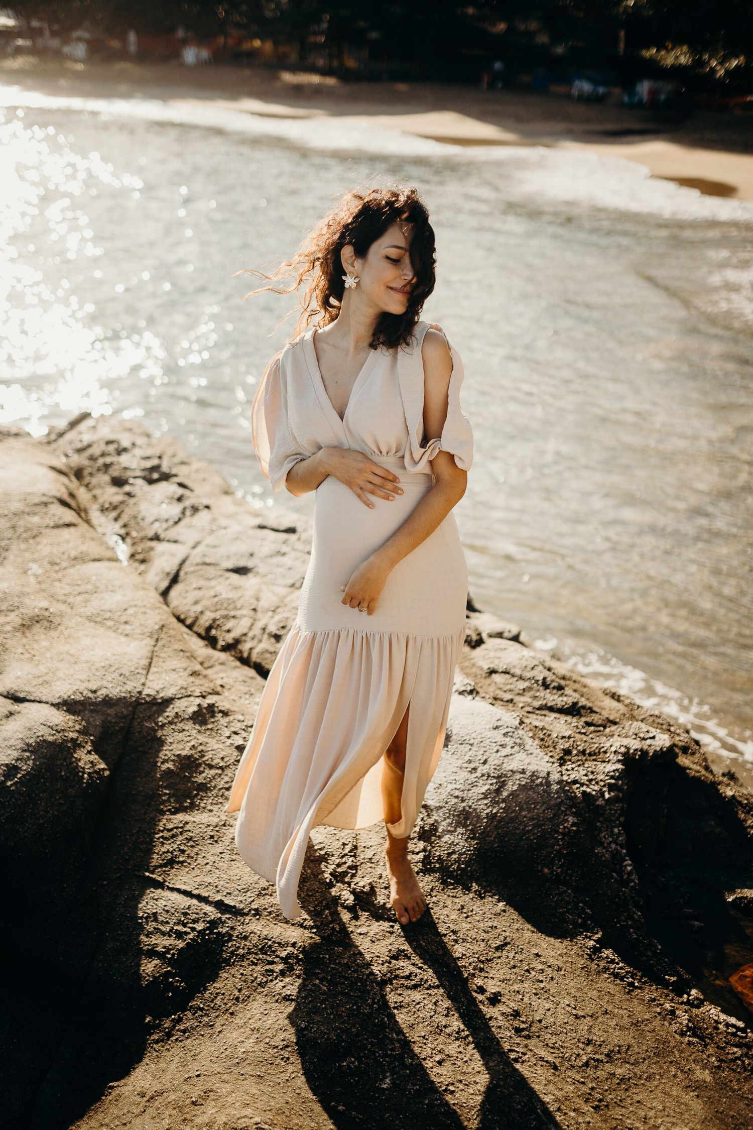 Romantic beachside maternity photos with dramatic shadows cast on rocky shoreline.