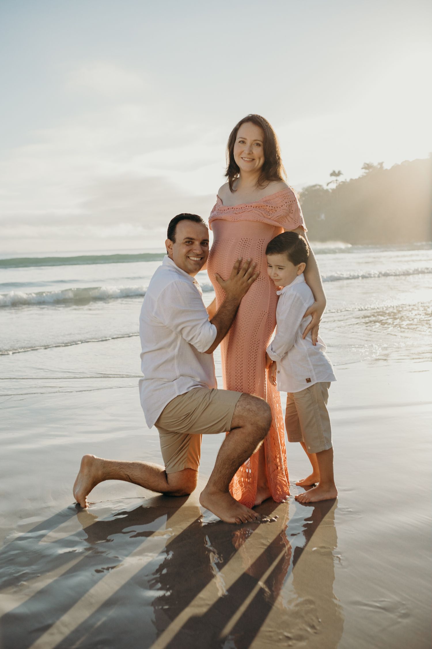 Family posing together on a sunny beach during sunset as waves roll in behind them.