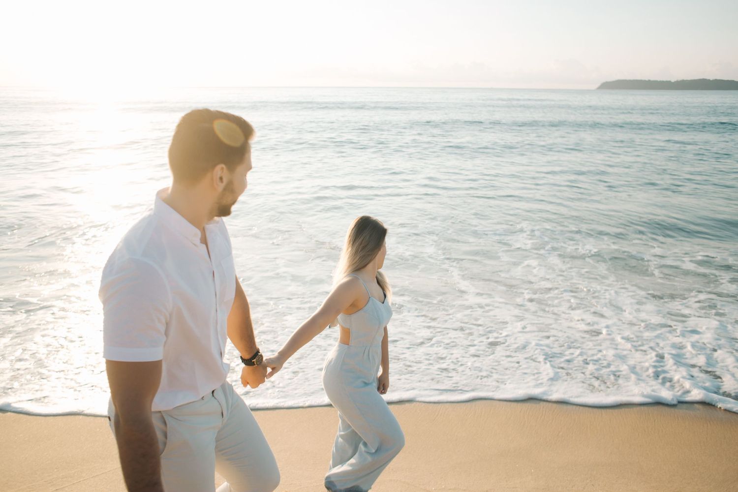 Couple walking along shoreline holding hands during golden hour at the beach.
