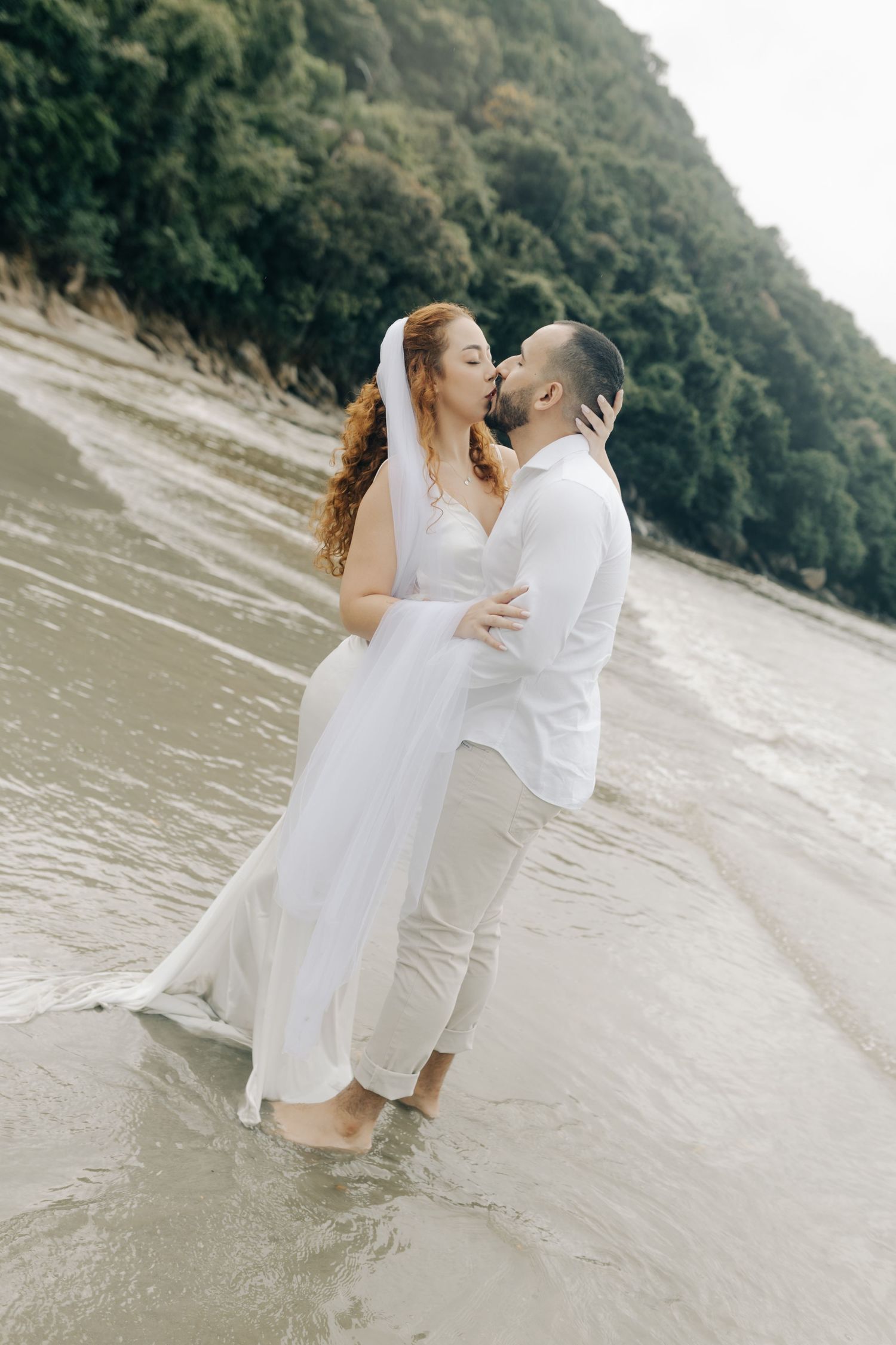 Romantic beach wedding moment with couple embracing near coastal cliffs.